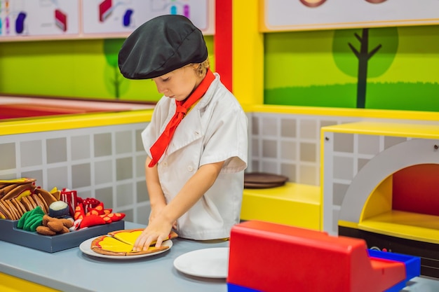 El niño juega en la cocina de juguete y cocina una pizza.