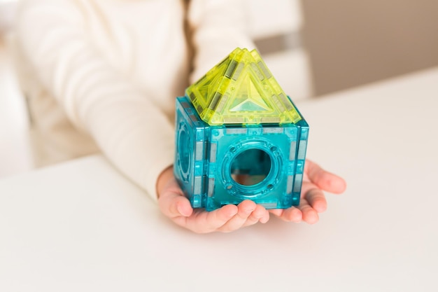 Un niño juega con un constructor magnético en una mesa blanca en casa o en el jardín de infantes Construyendo una casa de juguete con bloques Manos cerca