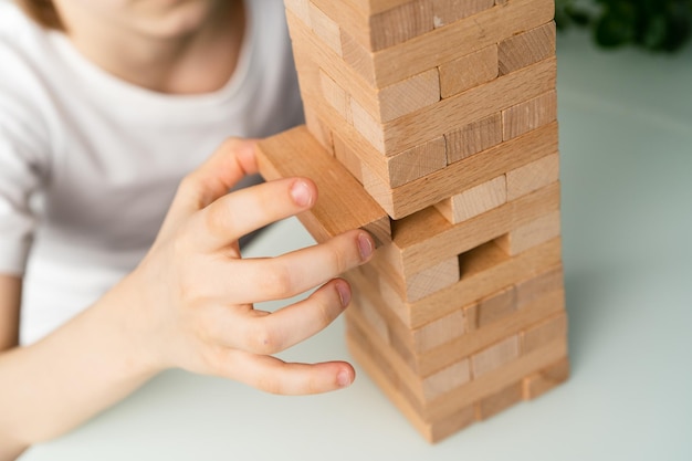 Un niño juega un juego de mesa construye una torre de cubos de madera con las manos cerca de un juego lógico de jenga para el desarrollo de un niño