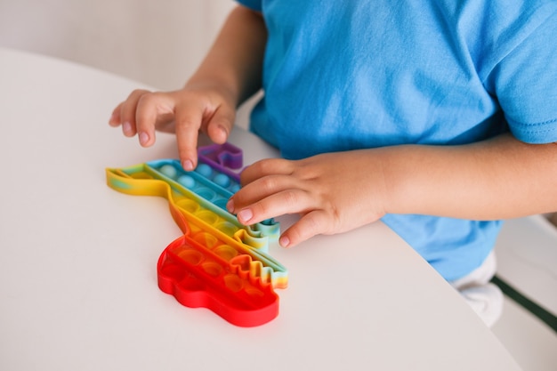 El niño juega con el juguete del arco iris Pop it fidget. Juego infantil antiestrés. Los juguetes de silicona de moda para niños lo hacen estallar para aliviar el estrés y desarrollar las habilidades motoras de las manos. Juguete de mano colorido con burbujas de empuje.