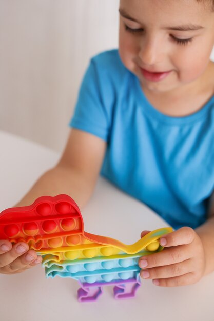 El niño juega con el juguete del arco iris Pop it fidget. Juego infantil antiestrés. Los juguetes de silicona de moda para niños lo hacen estallar para aliviar el estrés y desarrollar las habilidades motoras de las manos. Juguete de mano colorido con burbujas de empuje.