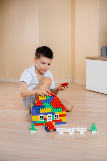 Un niño juega con un kit de construcción y construye una casa grande para toda la familia. Construcción de una vivienda familiar.