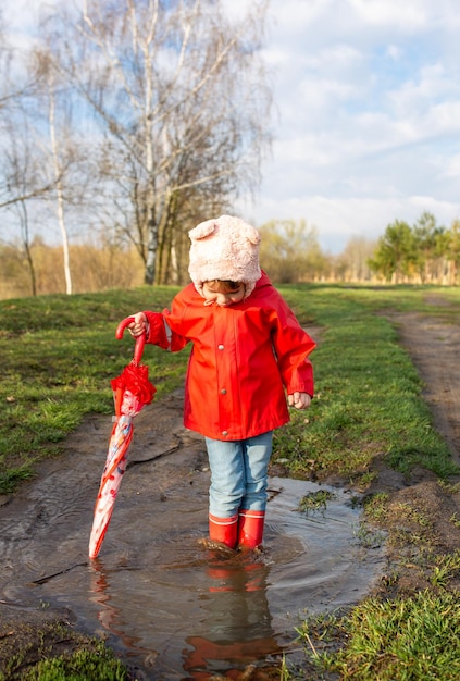 El niño juega con paraguas después de la lluvia con botas de goma rojas y un impermeable