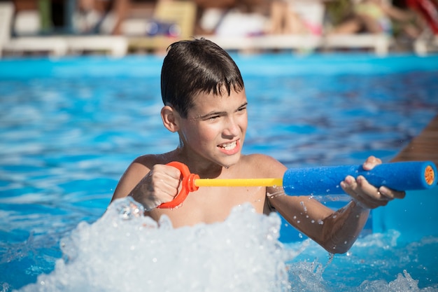 El niño juega en la piscina con una pistola de agua.