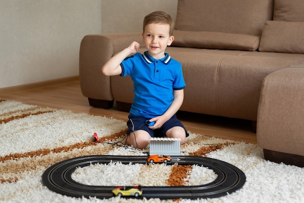 Niño juega con la pista de carreras en el control remoto en la alfombra