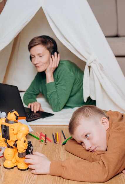 Niño juega robot mamá trabaja auriculares portátiles