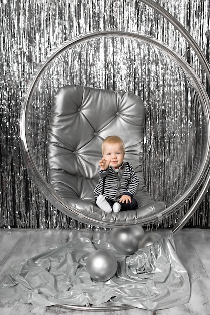 Niño juega en una silla un recipiente de vidrio con bolas de plata.