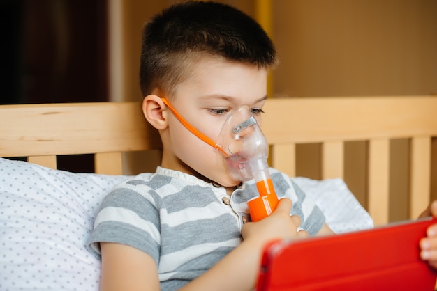 Foto un niño juega en una tableta durante un procedimiento de inhalación pulmonar. covid19, coronavirus, pandemia.