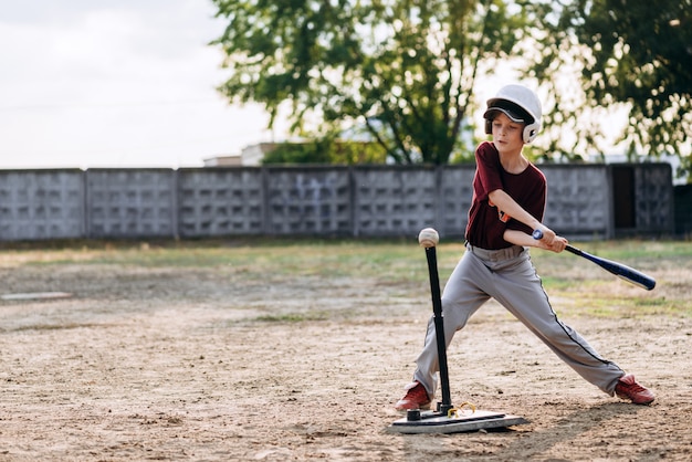 Un niño, un jugador de béisbol, golpea una pelota con un bate de béisbol