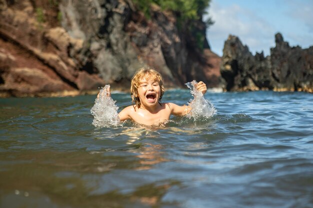 Niño jugando en el agua del océano niño saltando en las olas del mar vacaciones de los niños en la playa niño pequeño emocionado