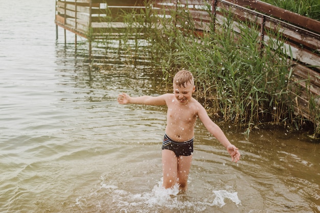 Niño jugando en el agua en la orilla de un lago. Vacaciones de verano.