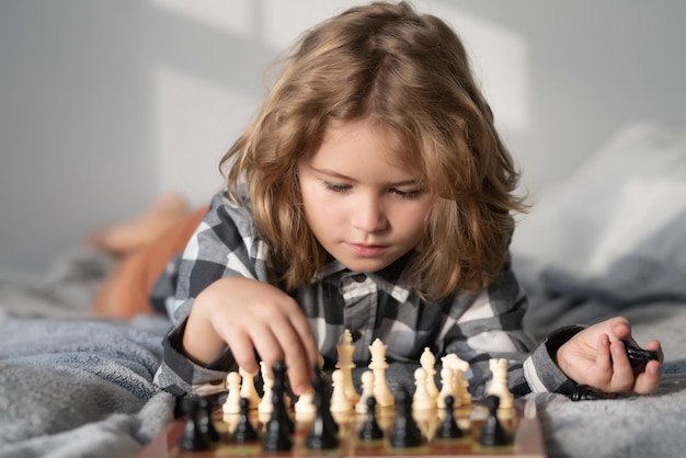 Niño jugando al ajedrez en la cama niño inteligente pensando en el desarrollo temprano de los niños de ajedrez