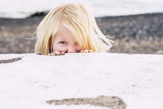 Niño jugando al escondite escondiéndose detrás de una estructura de hormigón en la playa. Niño juguetón jugando en la playa. Cute little boy jugando y mirando a través de un muro de hormigón al aire libre