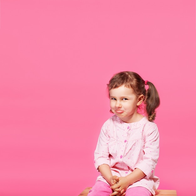 Niño jugando al mono. Hijita vistiendo ropa rosa contra un rosa