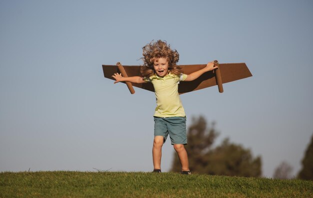 Niño jugando con alas de juguete en el fondo del cielo de verano