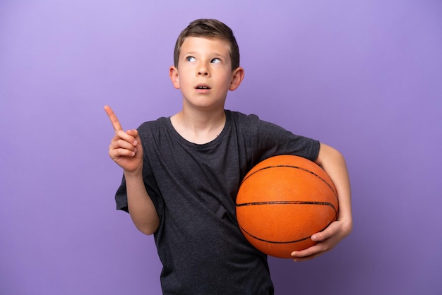 Niño jugando baloncesto aislado en un fondo morado pensando en una idea apuntando con el dedo hacia arriba