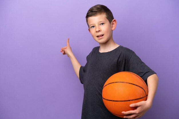 Niño jugando baloncesto aislado sobre fondo púrpura apuntando hacia atrás