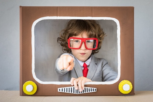 Niño jugando con caja de cartón TV. Niño divirtiéndose en casa. Concepto de blogs de video