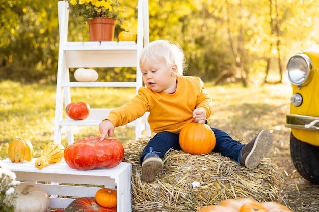 Niño jugando con calabaza en sus manos en el fondo del parque de otoño con árboles dorados