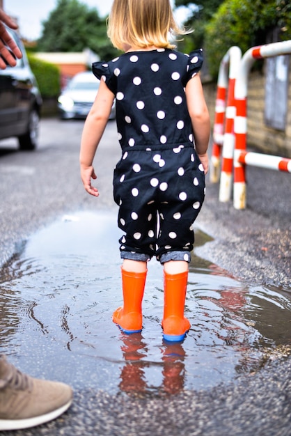 niño jugando en un charco con botas de goma después de la lluvia de verano