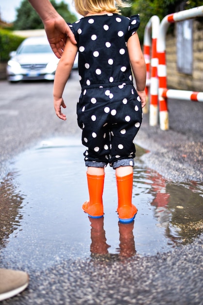 niño jugando en un charco con botas de goma después de la lluvia de verano