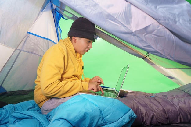 Niño jugando con una computadora portátil dentro de una carpa sobre un fondo verde