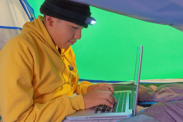 Niño jugando con una computadora portátil dentro de una carpa sobre un fondo verde