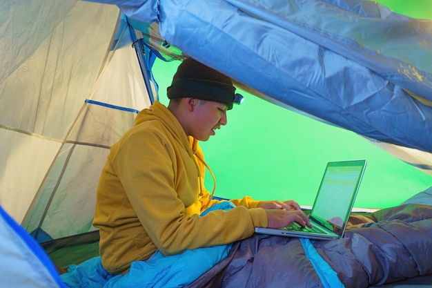 Niño jugando con una computadora portátil dentro de una carpa sobre un fondo verde