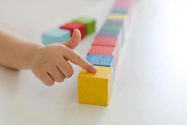 Niño jugando y construyendo con coloridos ladrillos de juguete de madera sobre una mesa de madera blanca aprendizaje temprano y