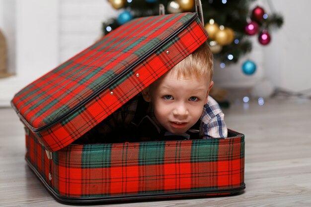 Niño jugando escondido en una maleta de cuadros rojos