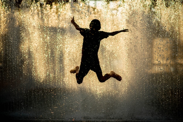 Niño jugando a la fuente de gotas de agua debajo de la tela y el paraguas