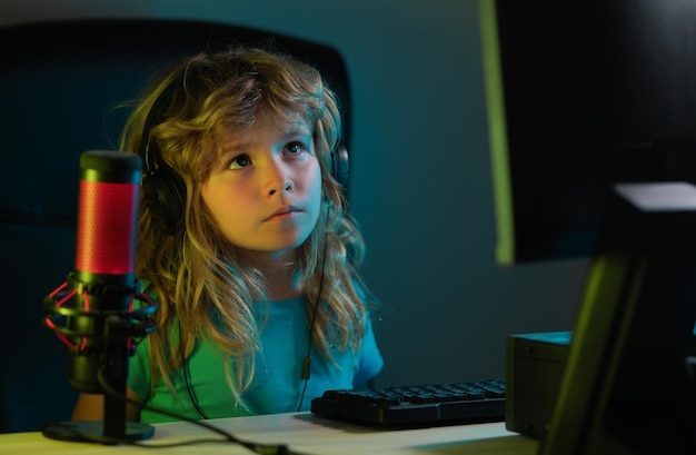 Niño jugando juegos de computadora o estudiando en la computadora de ordenador Niño jugador en la luz de neón de la noche