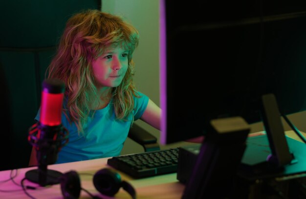 Niño jugando juegos de computadora o estudiando en una computadora PC Niño jugador en la noche iluminación de neón Concepto de educación a distancia Niños trabajando en línea jugando en una PC de escritorio