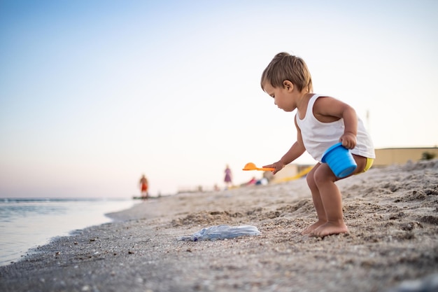 Niño jugando con juguetes en la playa construyendo cuentas y torretas sonriendo a alguien detrás de escena en las vacaciones de verano