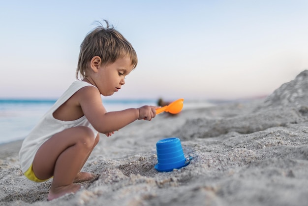 Niño jugando con juguetes en la playa construyendo cuentas y torretas sonriendo a alguien detrás de escena en las vacaciones de verano