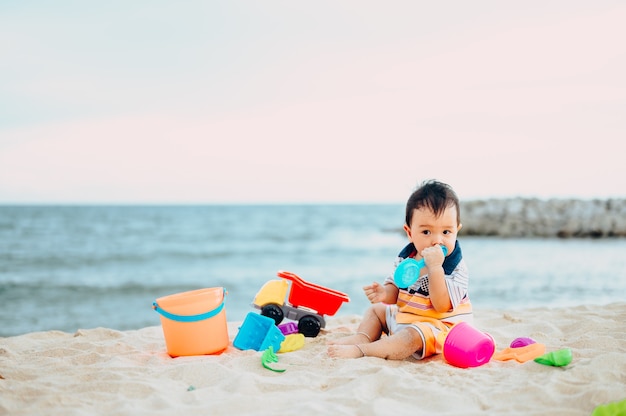 Niño jugando con juguetes de playa con su madre en la playa tropical.