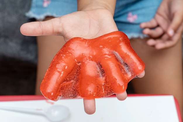 Niño jugando con limo de color rojo, gunge, gel en las manos