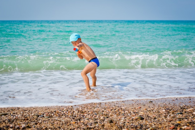 Niño jugando en el mar con pistola de agua