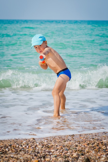 Niño jugando en el mar con pistola de agua