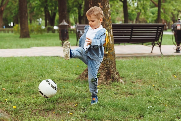 Niño jugando a la pelota en el parque golpea la pelota corre a través de los deportes de campo niños entrena al aire libre