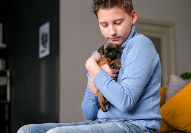 Niño jugando con un perro bebé. Los niños juegan con cachorros en casa. Niño pequeño y leonado o perro brabanson