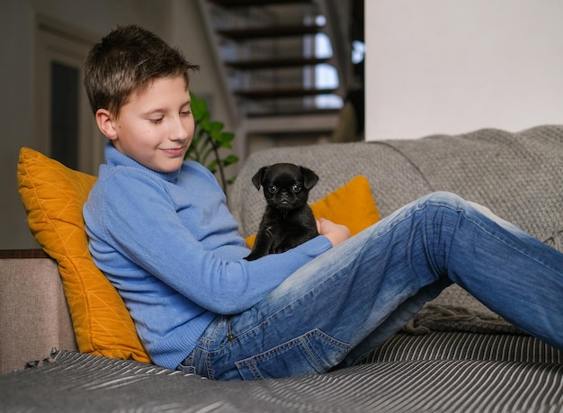 Niño jugando con un perro bebé. Los niños juegan con cachorros en casa. Niño pequeño y leonado o perro brabanson