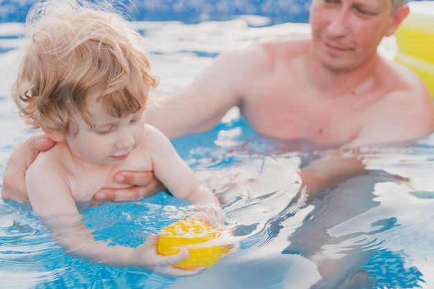 Niño jugando en la piscina y aprendiendo a nadar con su papá