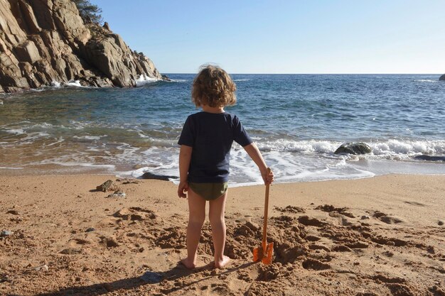 Foto niño jugando en la playa con una pala haciendo un agujero en la arena
