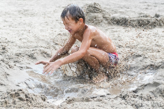 Niño jugando en la playa saltando en la arena mojada y sucia