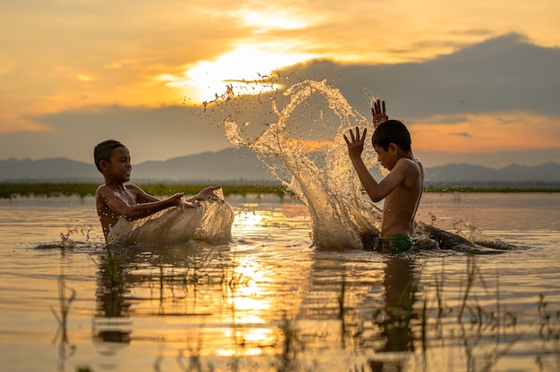 Niño jugando a salpicaduras de agua en el río durante la puesta de sol, salpicaduras de agua, Tailandia