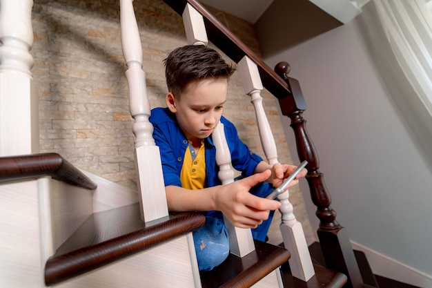 Niño jugando con smartphone, sentado en las escaleras. Vista desde arriba.