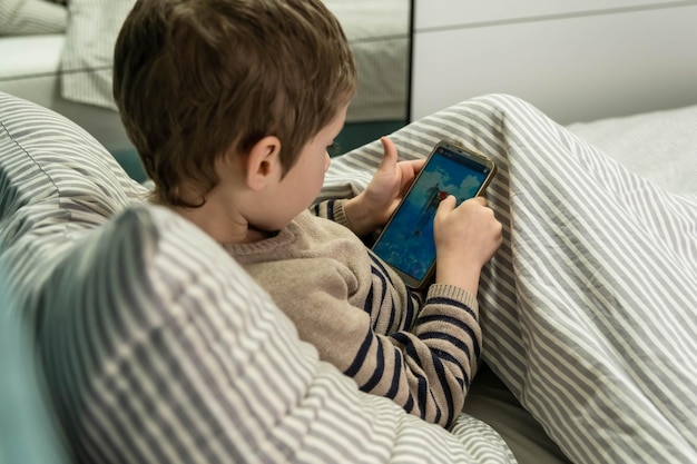 Niño jugando en el teléfono inteligente cómodamente sentado en la cama