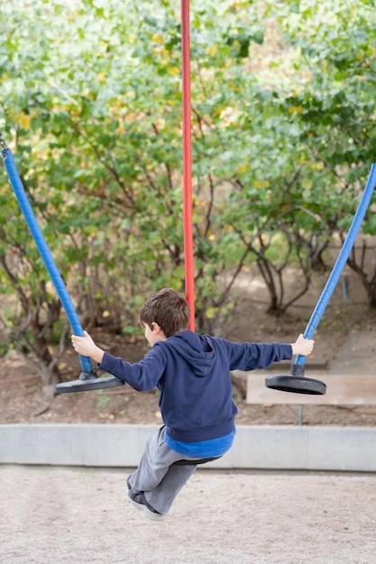 Niño jugando con tres cuerdas de columpio de colores en un parque Vista trasera