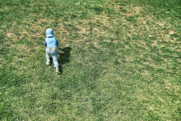 Un niño juguetón sube una empinada ladera cubierta de exuberante hierba verde en la vista trasera del parque